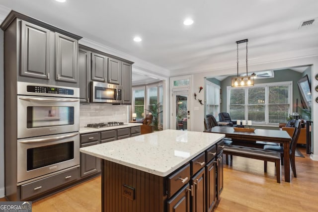 kitchen with stainless steel appliances, a center island, ornamental molding, dark brown cabinets, and hanging light fixtures