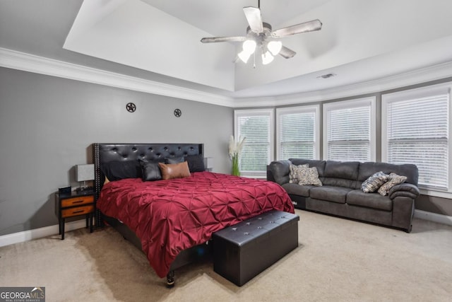 carpeted bedroom featuring ceiling fan, crown molding, multiple windows, and a tray ceiling