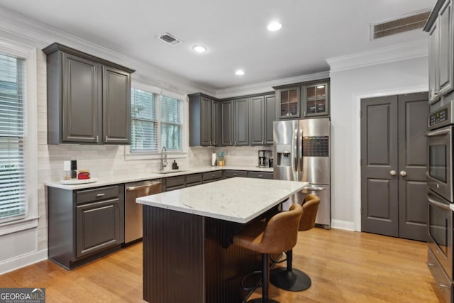 kitchen with appliances with stainless steel finishes, ornamental molding, light hardwood / wood-style floors, and a center island