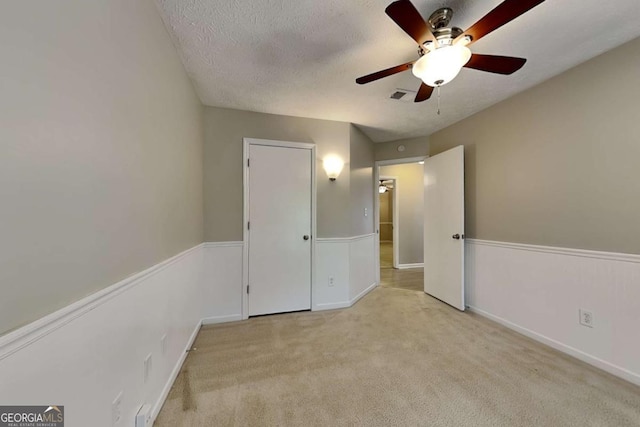 unfurnished bedroom featuring ceiling fan, light carpet, and a textured ceiling