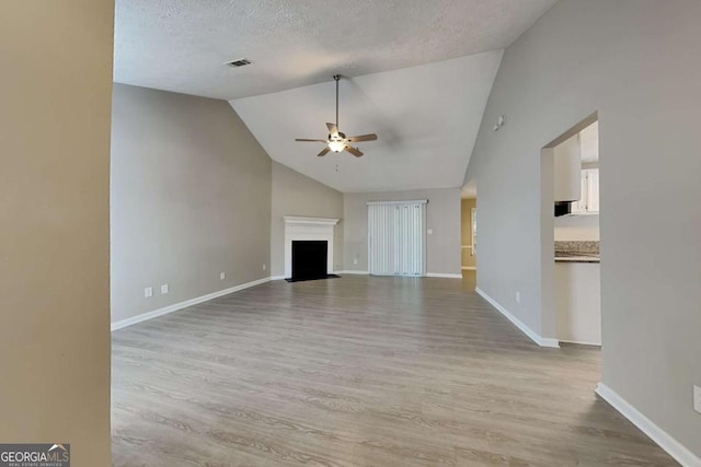 unfurnished living room featuring ceiling fan, light wood-type flooring, a textured ceiling, and lofted ceiling