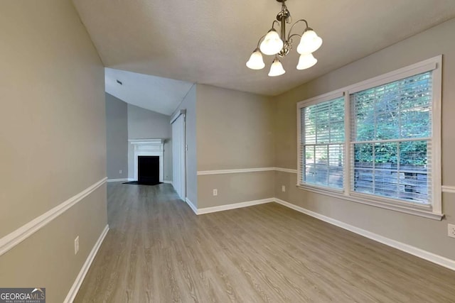 unfurnished room featuring hardwood / wood-style floors, lofted ceiling, and an inviting chandelier