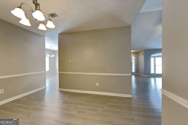 unfurnished room featuring a chandelier, a textured ceiling, and wood-type flooring