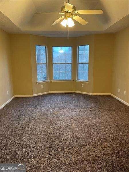 unfurnished room with a raised ceiling, carpet flooring, and ceiling fan