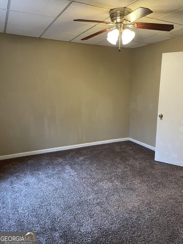 carpeted empty room with ceiling fan and a drop ceiling