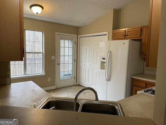 kitchen featuring white refrigerator with ice dispenser, sink, lofted ceiling, and a textured ceiling