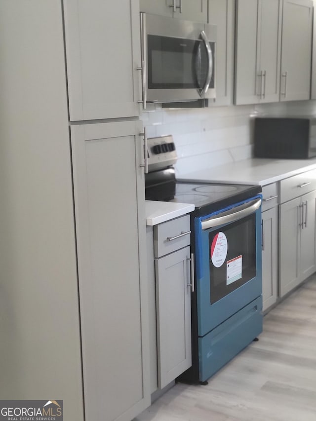 kitchen with stainless steel appliances, gray cabinets, and light hardwood / wood-style flooring