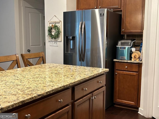 kitchen featuring decorative backsplash, dark hardwood / wood-style flooring, light stone countertops, and stainless steel refrigerator with ice dispenser