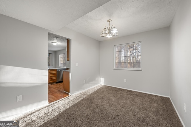 carpeted empty room featuring a healthy amount of sunlight, an inviting chandelier, and a textured ceiling