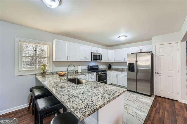 kitchen featuring white cabinets, sink, light stone countertops, appliances with stainless steel finishes, and kitchen peninsula