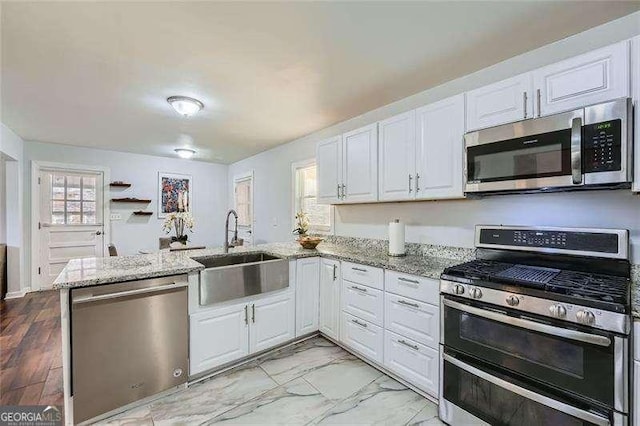 kitchen featuring kitchen peninsula, light stone counters, stainless steel appliances, sink, and white cabinets