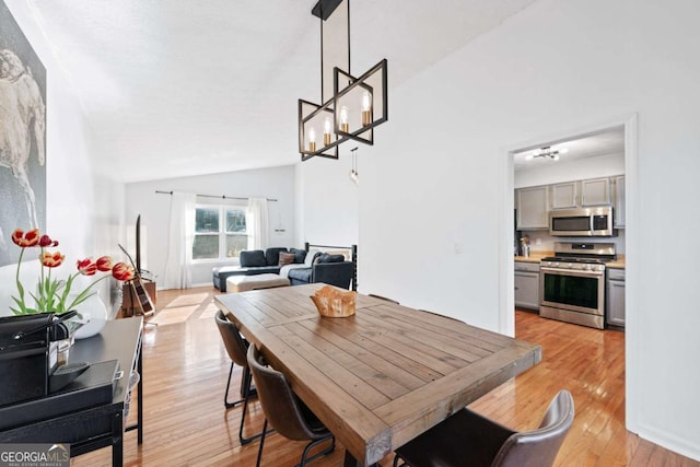 dining area with light wood-type flooring, vaulted ceiling, and a chandelier