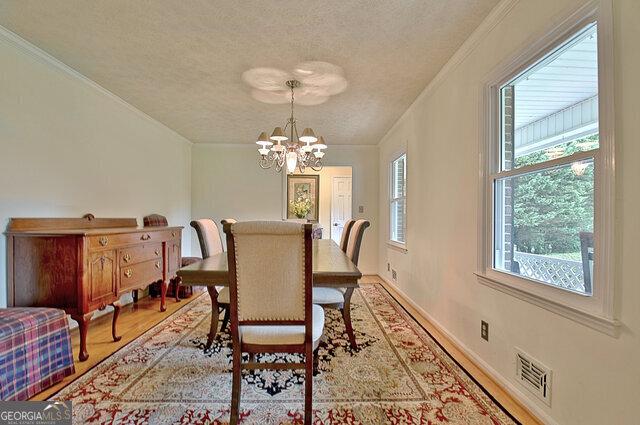 dining space featuring ornamental molding, a textured ceiling, light hardwood / wood-style floors, and a notable chandelier