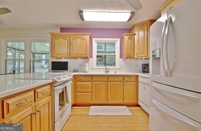 kitchen featuring light brown cabinetry, sink, light hardwood / wood-style floors, and white appliances