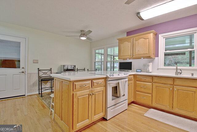 kitchen featuring kitchen peninsula, light hardwood / wood-style flooring, white range with electric stovetop, and a wealth of natural light