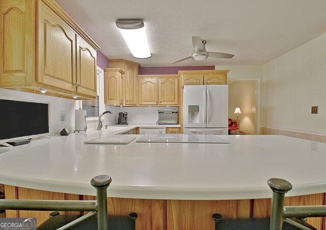 kitchen featuring white fridge with ice dispenser, sink, a kitchen breakfast bar, kitchen peninsula, and light brown cabinetry