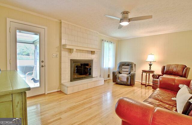 living room featuring ornamental molding, a textured ceiling, ceiling fan, a fireplace, and hardwood / wood-style floors