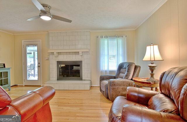 living room featuring a fireplace, light hardwood / wood-style floors, ceiling fan, and crown molding