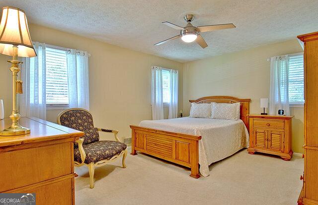 bedroom with ceiling fan, light colored carpet, a textured ceiling, and multiple windows