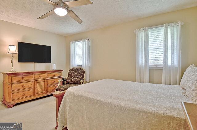 carpeted bedroom featuring ceiling fan and a textured ceiling