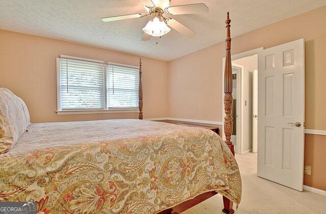 bedroom with ceiling fan, light colored carpet, and a textured ceiling