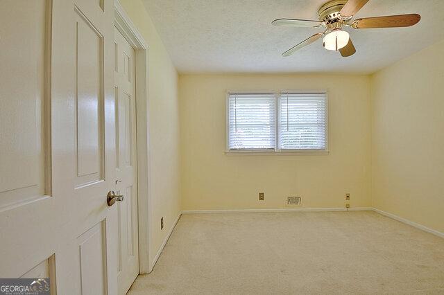 empty room with ceiling fan, light colored carpet, and a textured ceiling