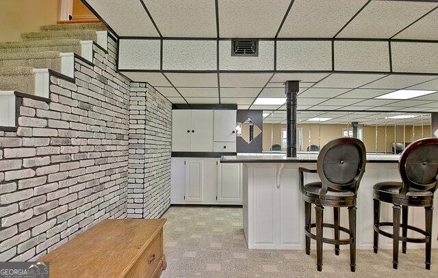 kitchen with white cabinets, a drop ceiling, a breakfast bar area, and brick wall