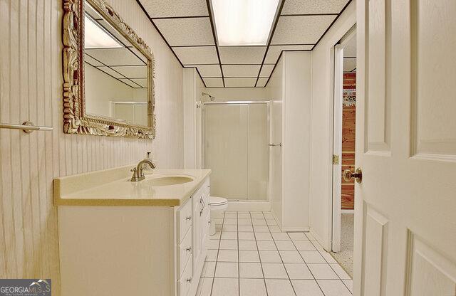 bathroom featuring a paneled ceiling, vanity, tile patterned floors, toilet, and a shower with shower door