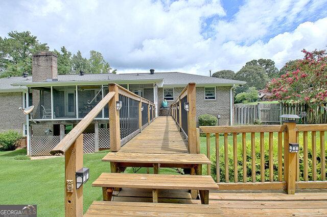 back of property featuring a lawn, a sunroom, and a wooden deck