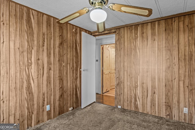 carpeted spare room featuring ceiling fan and wooden walls