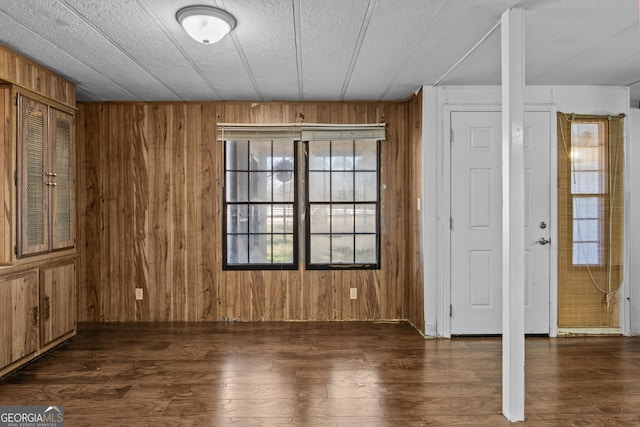 unfurnished room with a healthy amount of sunlight, a textured ceiling, dark wood-type flooring, and wooden walls