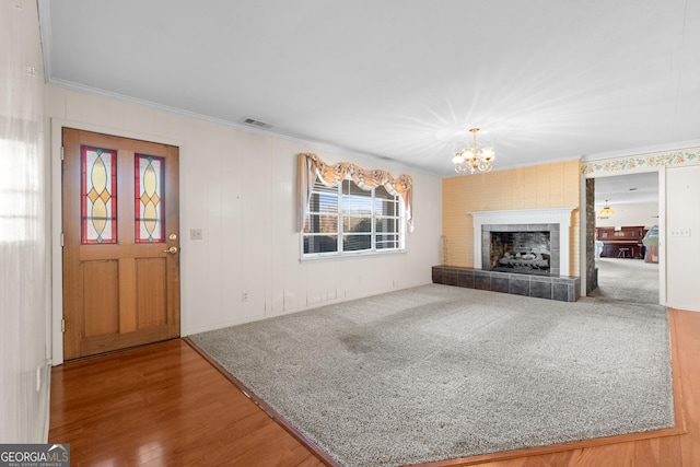 unfurnished living room with a tile fireplace, hardwood / wood-style flooring, crown molding, and a notable chandelier