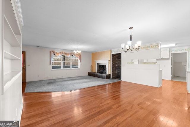 unfurnished living room with light wood-type flooring, a large fireplace, an inviting chandelier, and crown molding