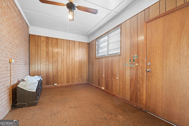 carpeted empty room with ceiling fan, brick wall, wood walls, and ornamental molding