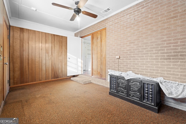 unfurnished bedroom with ornamental molding, ceiling fan, wooden walls, and brick wall