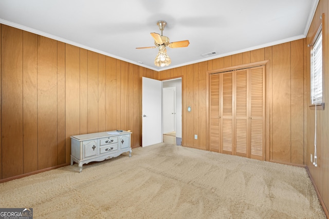 unfurnished bedroom featuring wooden walls, a closet, ceiling fan, and crown molding