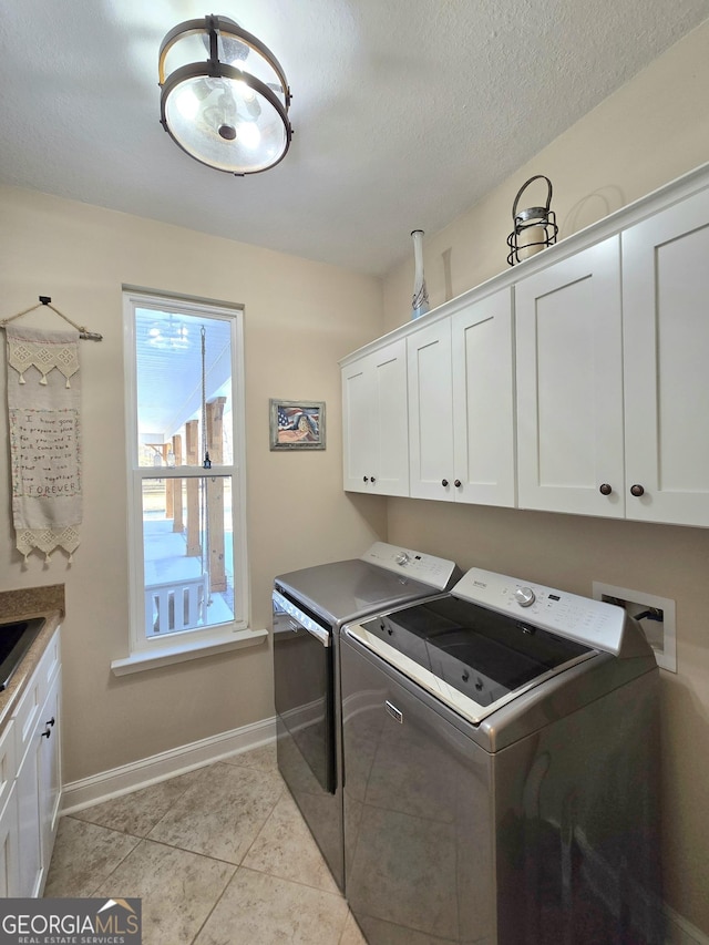 clothes washing area featuring washing machine and dryer, light tile patterned floors, cabinets, and a textured ceiling