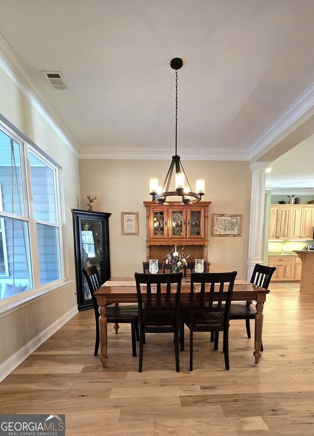 dining space with decorative columns, crown molding, a chandelier, and light wood-type flooring