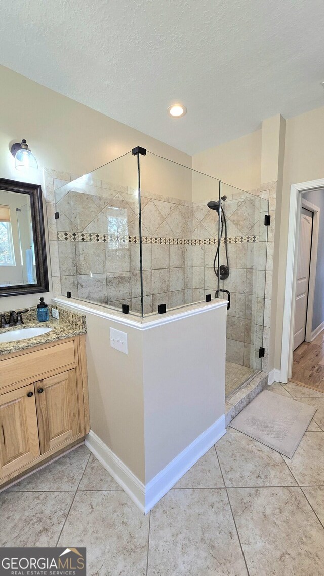 bathroom with tile patterned floors, vanity, a shower with shower door, and a textured ceiling