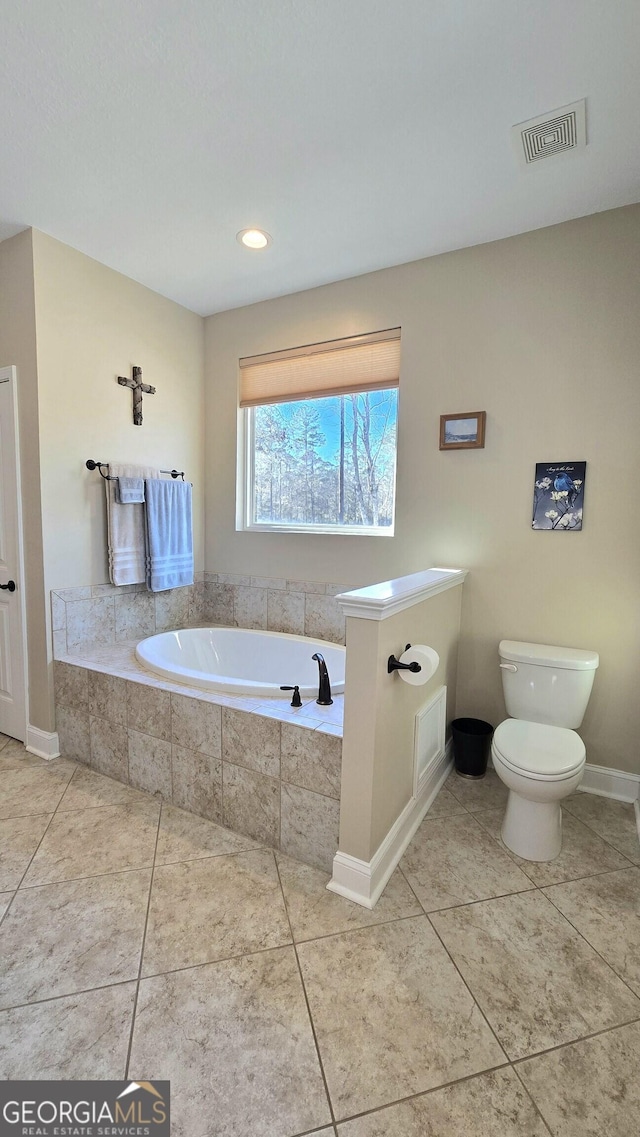 bathroom featuring tile patterned floors, tiled bath, and toilet