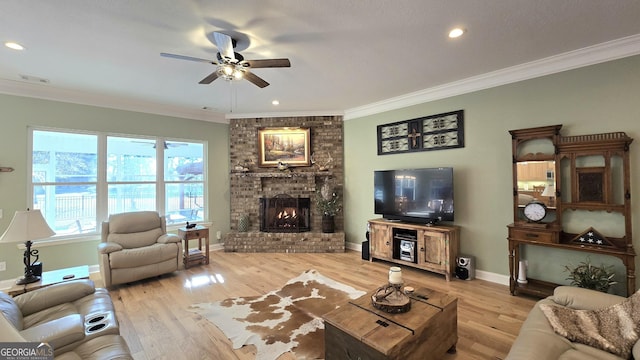 living room featuring ceiling fan, crown molding, light hardwood / wood-style flooring, and a brick fireplace