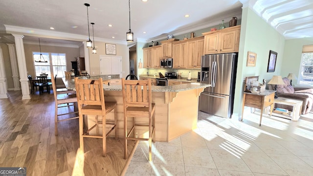 kitchen featuring hanging light fixtures, light stone countertops, appliances with stainless steel finishes, a large island, and decorative columns