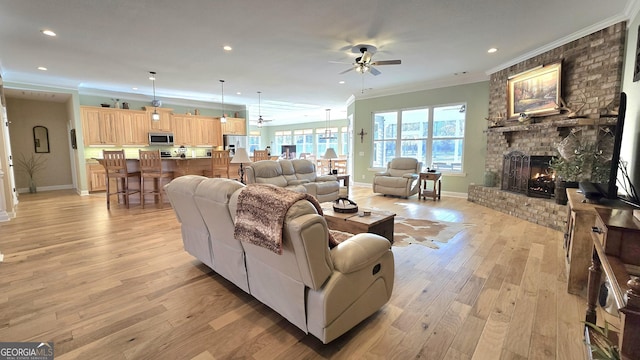 living room featuring ceiling fan, crown molding, a fireplace, and light hardwood / wood-style flooring