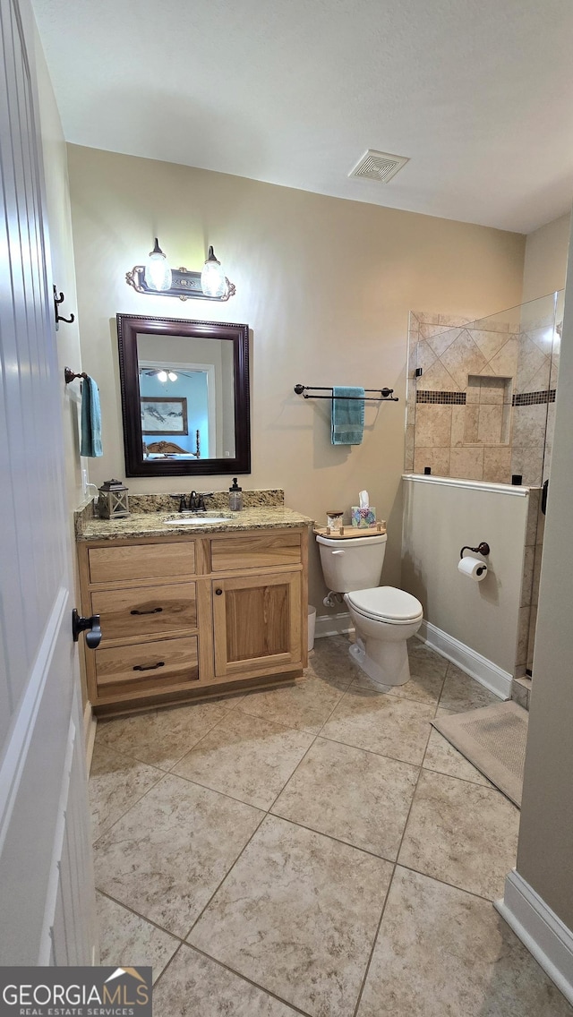 bathroom featuring a tile shower, tile patterned flooring, vanity, and toilet