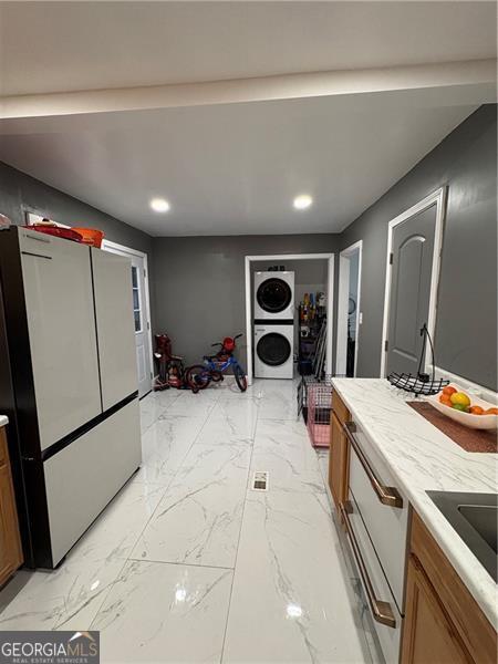 kitchen with stacked washer / drying machine, stainless steel fridge, and sink