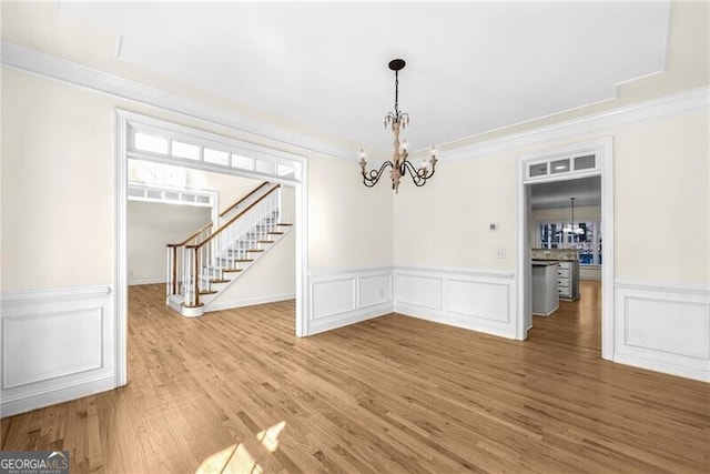 unfurnished dining area with hardwood / wood-style flooring, crown molding, and a chandelier