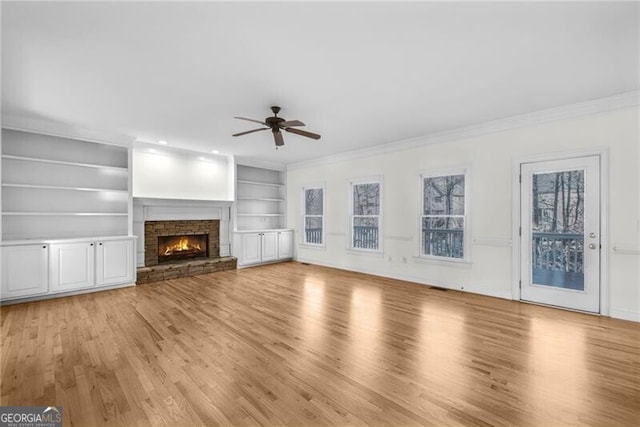 unfurnished living room featuring ceiling fan, light wood-type flooring, built in features, a fireplace, and ornamental molding