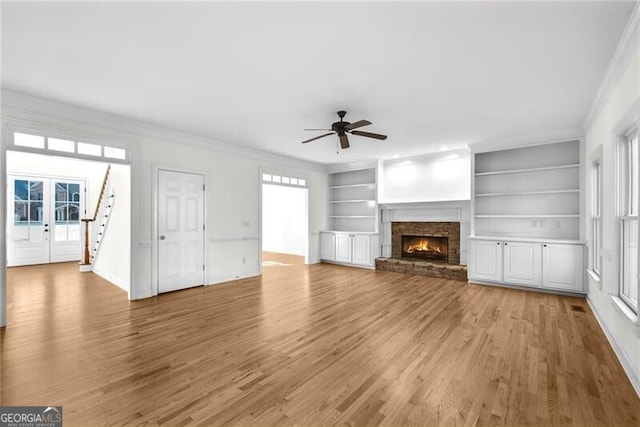 unfurnished living room featuring ceiling fan, french doors, built in features, a fireplace, and ornamental molding