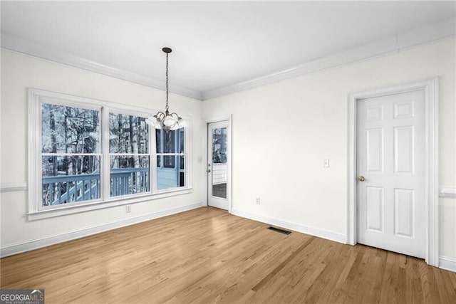 unfurnished dining area featuring hardwood / wood-style flooring, crown molding, and an inviting chandelier