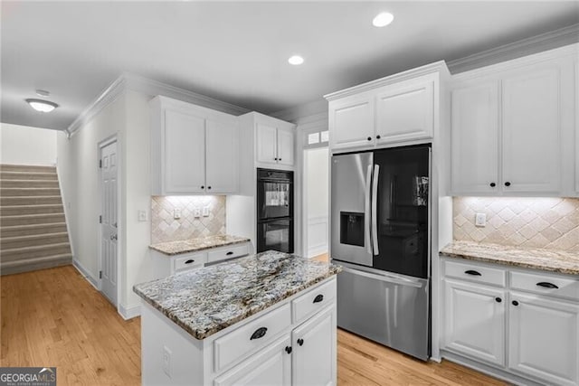 kitchen with white cabinets, stainless steel fridge, black double oven, and light hardwood / wood-style floors